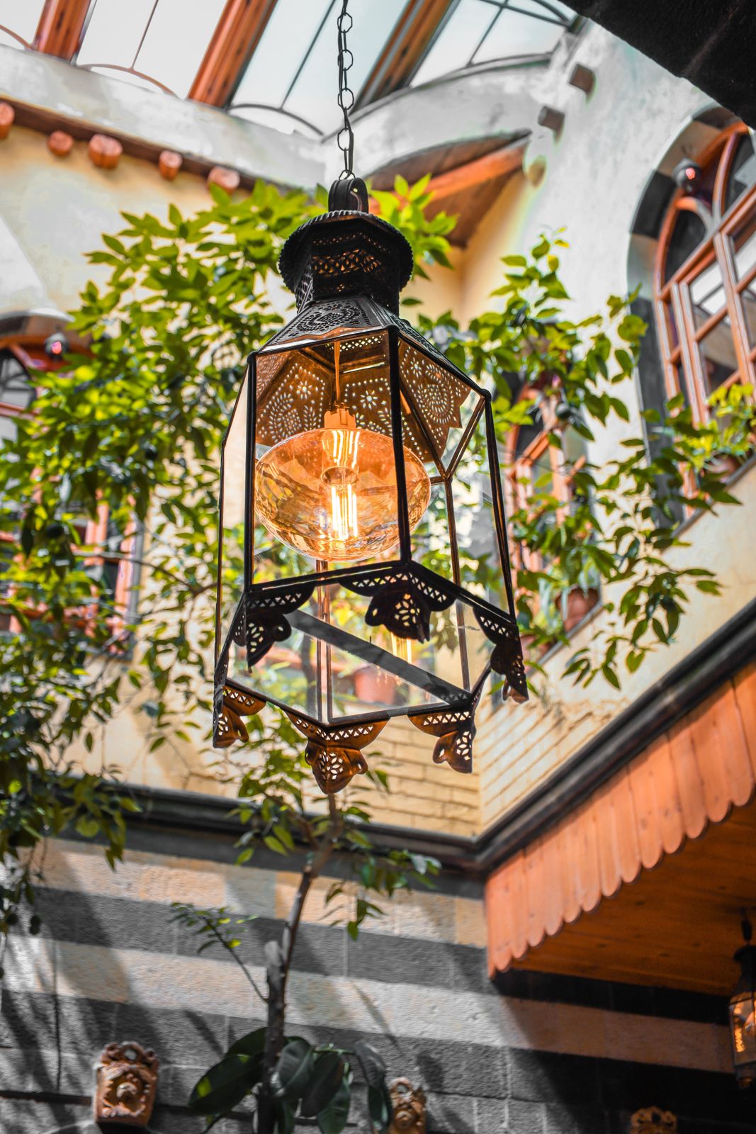 Hexagonal hanging lantern with pierced brass filigree, clear glass panels and a large amber filament globe bulb.